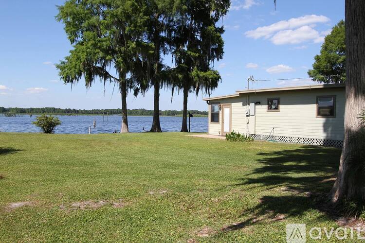 A house with a green lawn and trees in front of a body of water.
