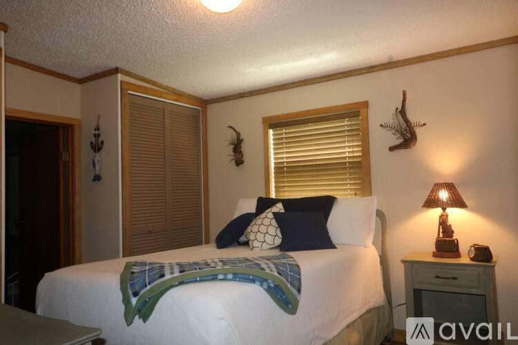 A bedroom with a bed, a nightstand with a lamp, and a window with blinds.