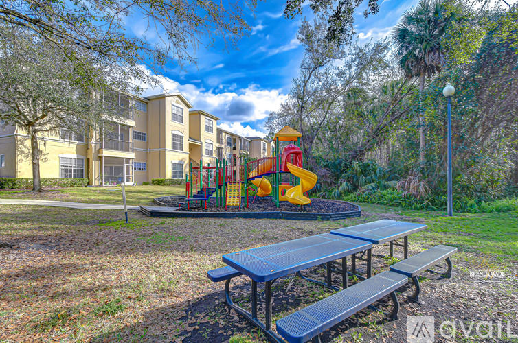 A playground with a slide and picnic tables in front of a building.