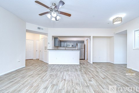 A spacious living room with a kitchen in the background and hardwood floors.