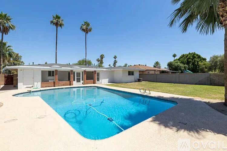 A pool in a backyard with a house and palm trees in the background.