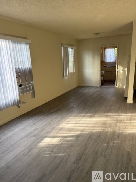 A spacious room with wooden flooring and a window with blinds.