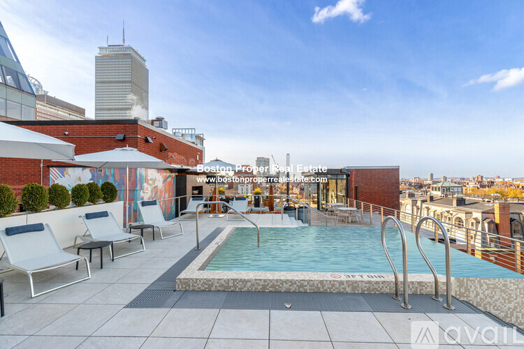 A rooftop pool area with lounge chairs and a view of the city skyline.