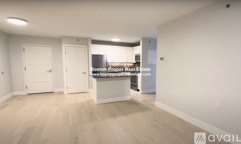 A spacious room with white walls and wooden flooring, featuring three white doors.