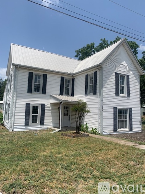 A white house with a grey roof and black shutters.