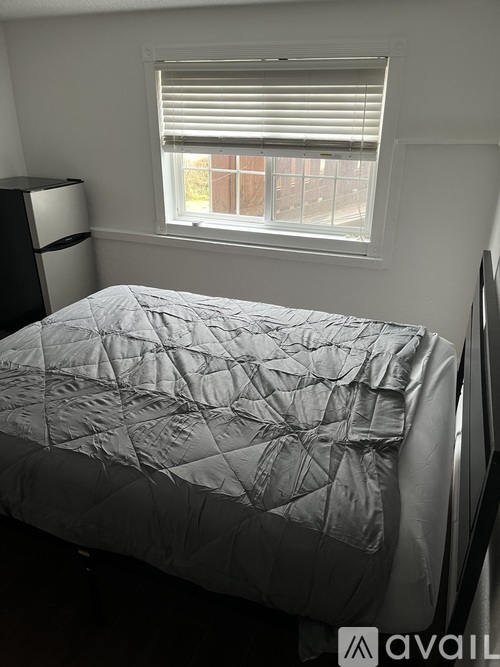 A bed with a white comforter sits in a room with a window.