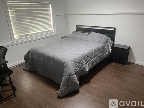 A bed with a grey comforter and a black headboard is in a room with a window and a wooden floor.