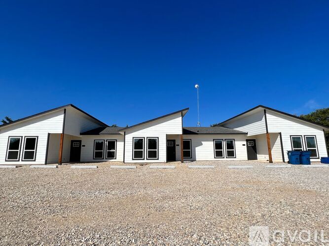 A white building with a blue container in front.