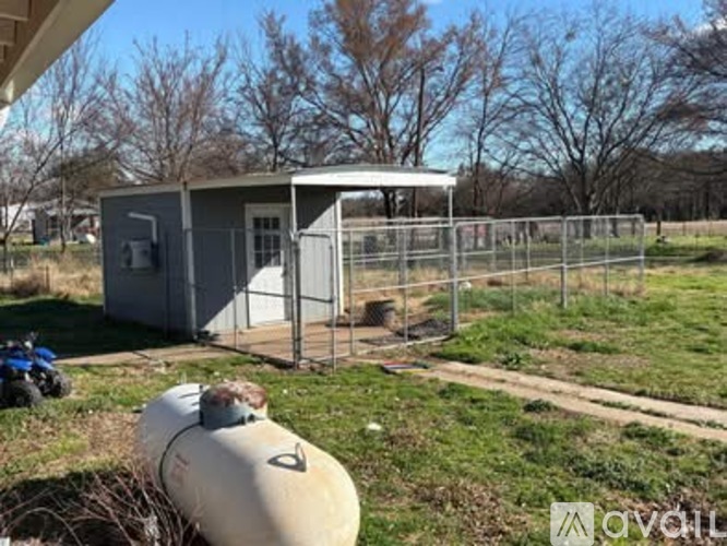 A small grey building with a white door and windows is surrounded by a fence and a large cylindrical tank is in the foreground.