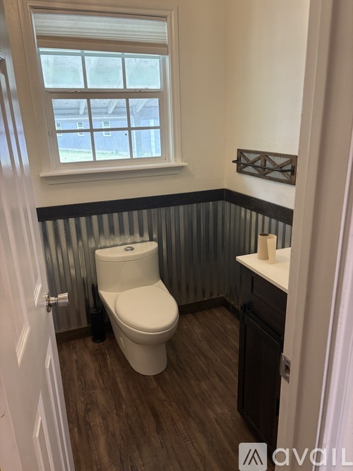 A white toilet in a bathroom with a window and a wooden floor.