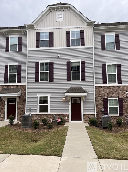 A grey two story apartment building with a red door and a small front yard.