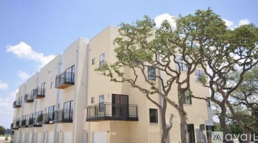 A beige apartment building with balconies and trees in front.