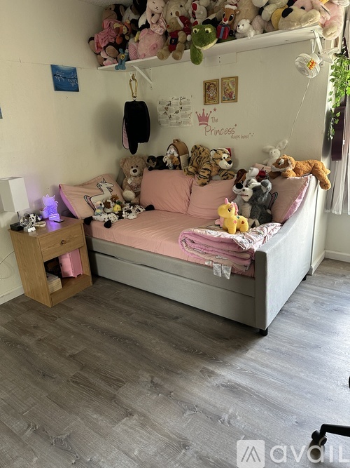 A child's bedroom with a bed covered in stuffed animals and a pink blanket.