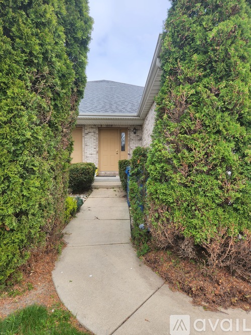 A house with a grey roof and a beige door is surrounded by green bushes.