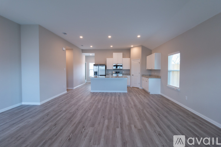 A spacious room with wooden flooring and a kitchen area in the background.