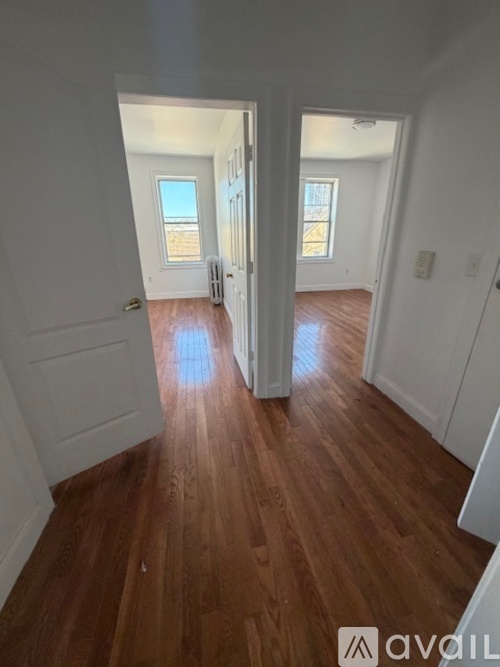 A hallway with wooden floors and white walls leading to two doors.