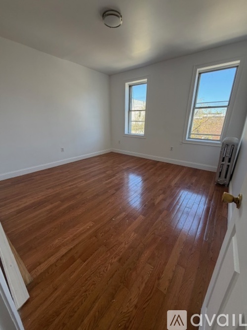 A room with wooden flooring and two windows.