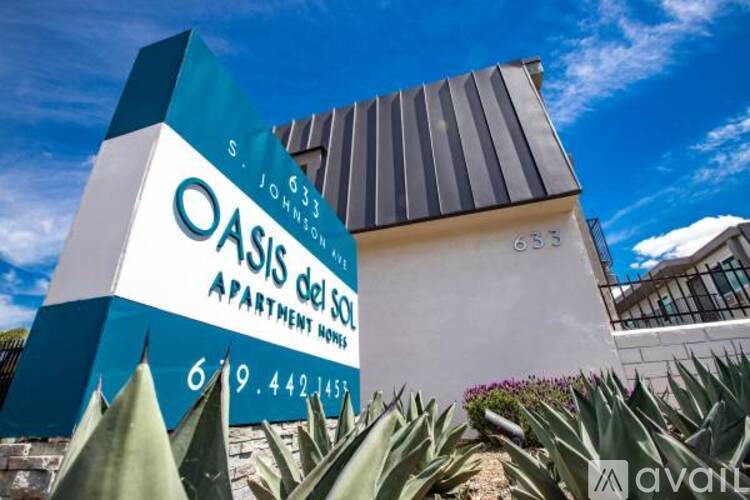 A blue and white sign for Oasis del Sol Apartment Homes stands in front of a building.