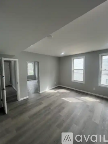 A room with grey walls and wooden flooring with a window on the right side.