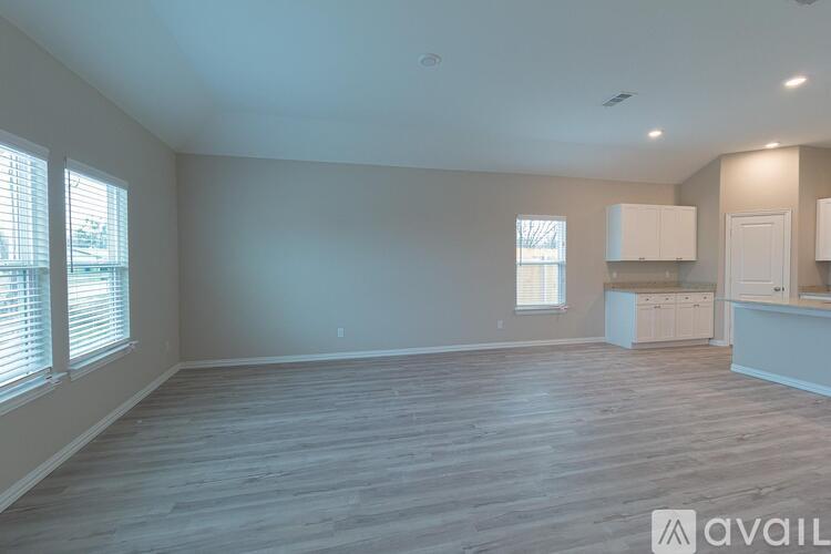 A spacious room with wooden flooring and a kitchen area with cabinets and a countertop.