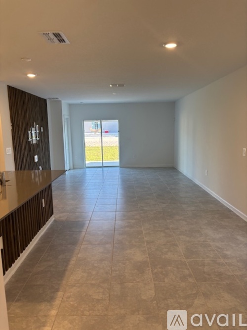 A spacious room with tiled flooring and a view of the outdoors through a sliding glass door.