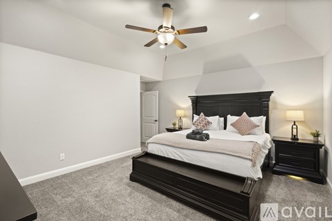 A bedroom with a large bed, a ceiling fan, and a nightstand with a lamp.
