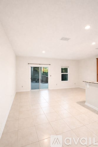 A spacious room with a tiled floor and a glass door leading to a balcony.