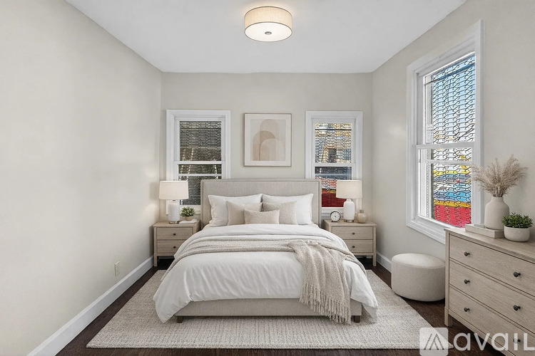 A bedroom with a large bed, two nightstands, and a window with a view of a cityscape.