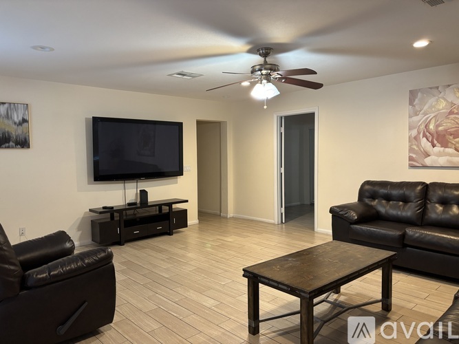 A living room with a black leather couch, a wooden coffee table, and a flat screen TV mounted on the wall.