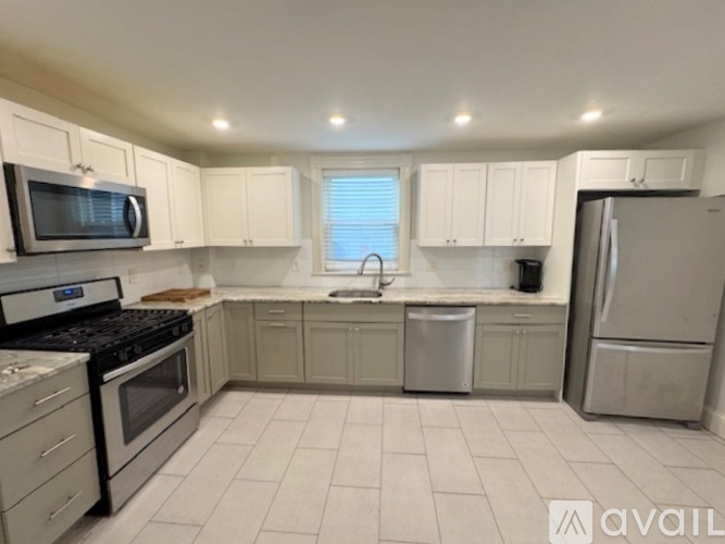 A kitchen with white cabinets and appliances, a window with blinds, and a sink with a faucet.