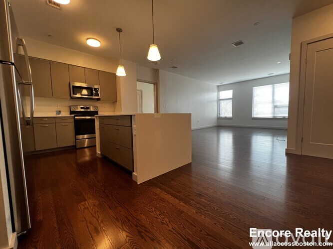 A kitchen with wooden floors and a refrigerator on the left.