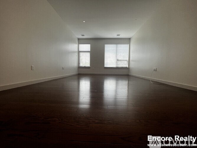 A spacious room with wooden floors and two windows.