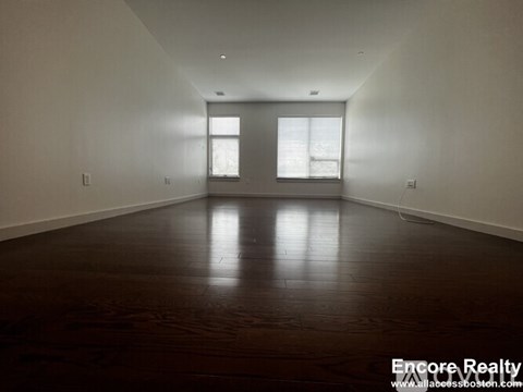 A spacious room with wooden floors and two windows.