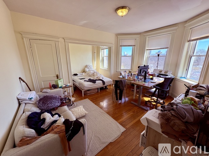 A messy living room with a couch, chair, and bed.
