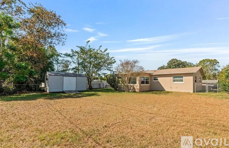 A house with a white garage door is situated in a field with trees in the background.
