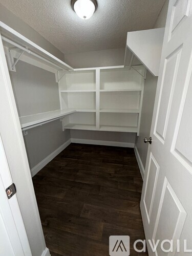 A white closet with shelves and a wooden floor.