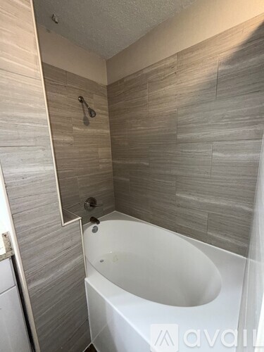 A bathroom with a white bathtub and grey tiled walls.