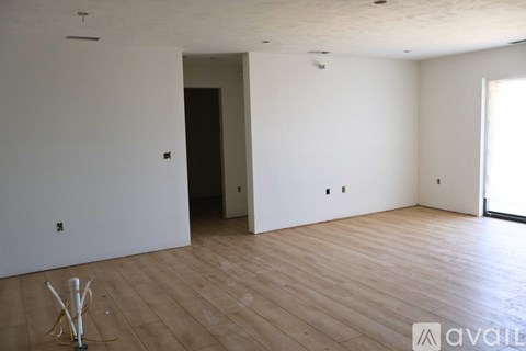 A room with wooden flooring and a white wall with a doorway leading to another room.