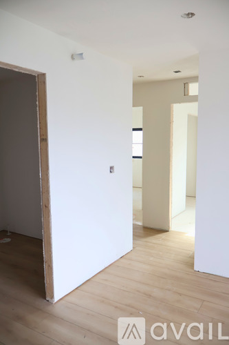 A room with a wooden floor and white walls with a door open to another room.