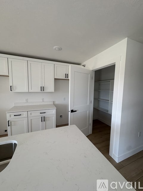 A room with a wooden floor and white walls with a door open to another room.