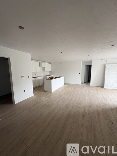 A room with wooden flooring and a white wall with a doorway leading to another room.