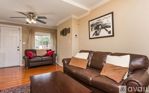 A living room with a brown leather couch and a ceiling fan.