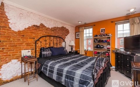 A bedroom with a brick wall and a bed with a plaid comforter.