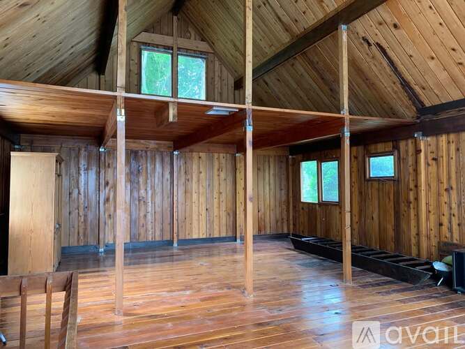A spacious room with wooden walls and ceiling, and a large window on the right wall.
