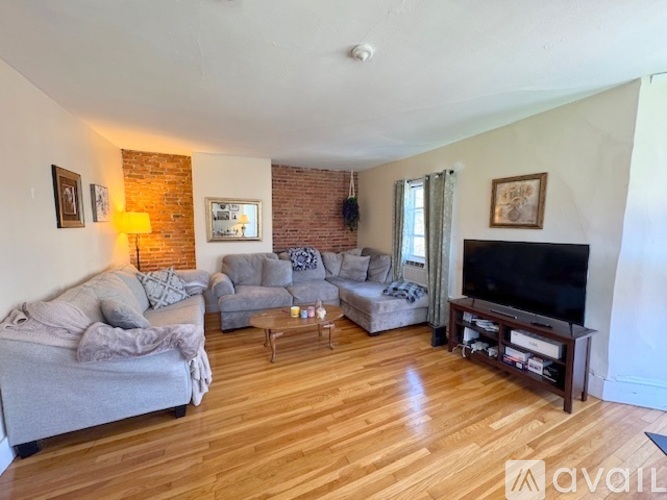 A living room with a grey couch, a grey armchair, a wooden coffee table, and a television on a wooden stand.