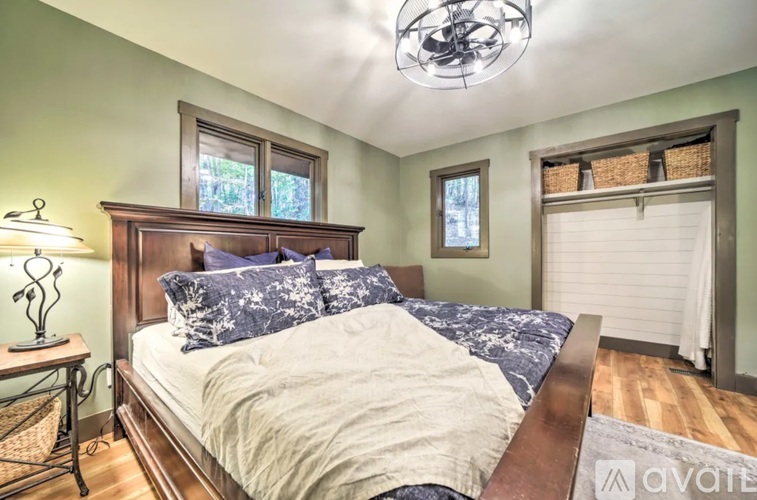 A bedroom with a bed, a nightstand with a lamp, and a window with blinds.
