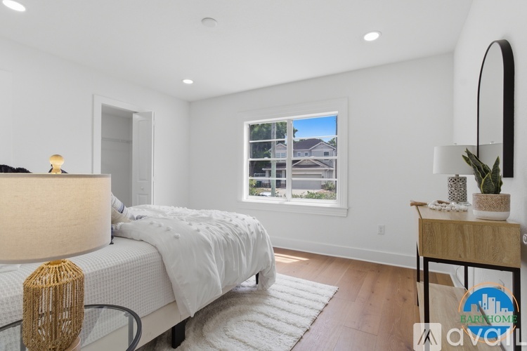 A well-lit bedroom with a large bed and a window overlooking a house.