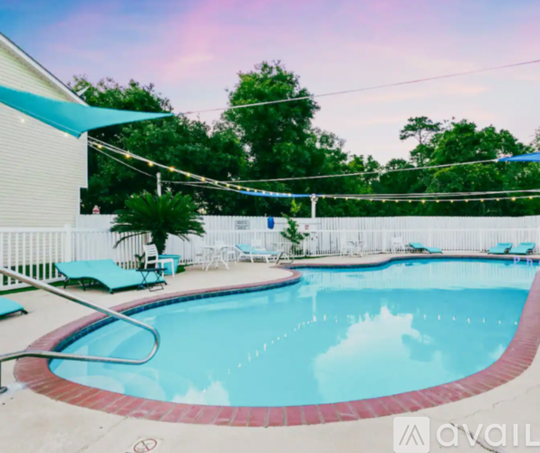 A swimming pool surrounded by a white fence and blue lounge chairs.