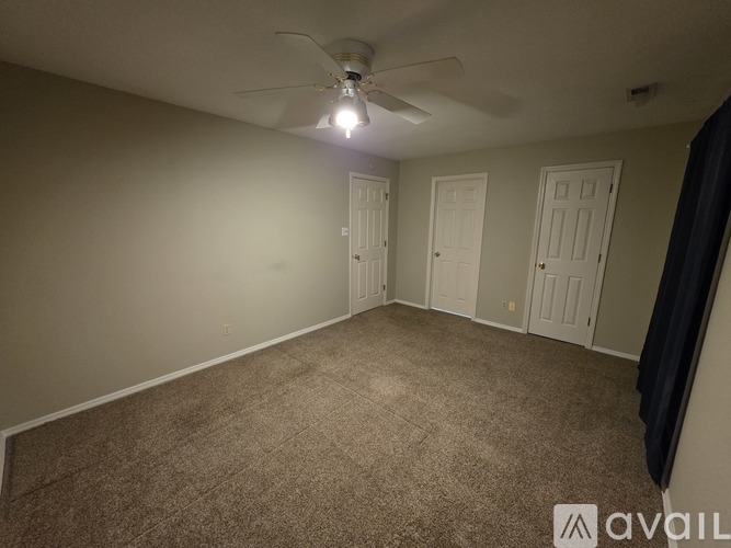 A room with a carpeted floor and a ceiling fan with a light on.