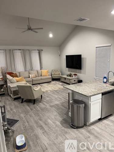 A modern living room with a grey sofa set, a television, and a kitchenette.